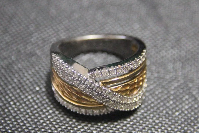 A three-band wrap ring with textured gold, smooth yellow gold, and silver bands, set against a dark gray textured background.