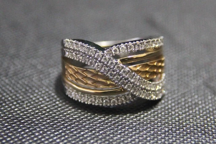 A two-tone ring with a textured gold band and silver pavé-set bands, resting on a textured gray surface.